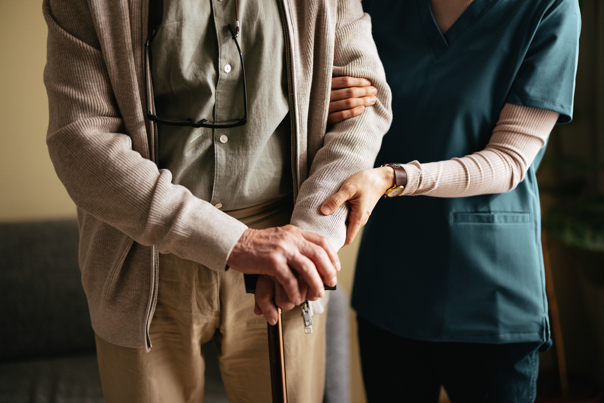 A care worker in dark teal supporting an older adult.